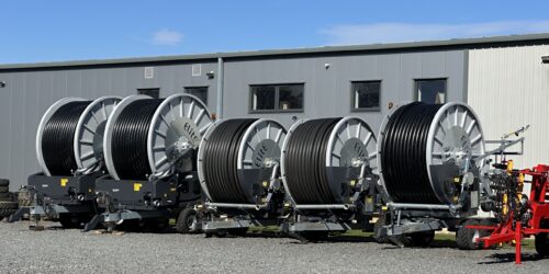 A row of new irrigation reels neatly lined up against a grey building backdrop