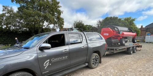A grey truck with a red Kempter C30 Grass pick up header on the bed.